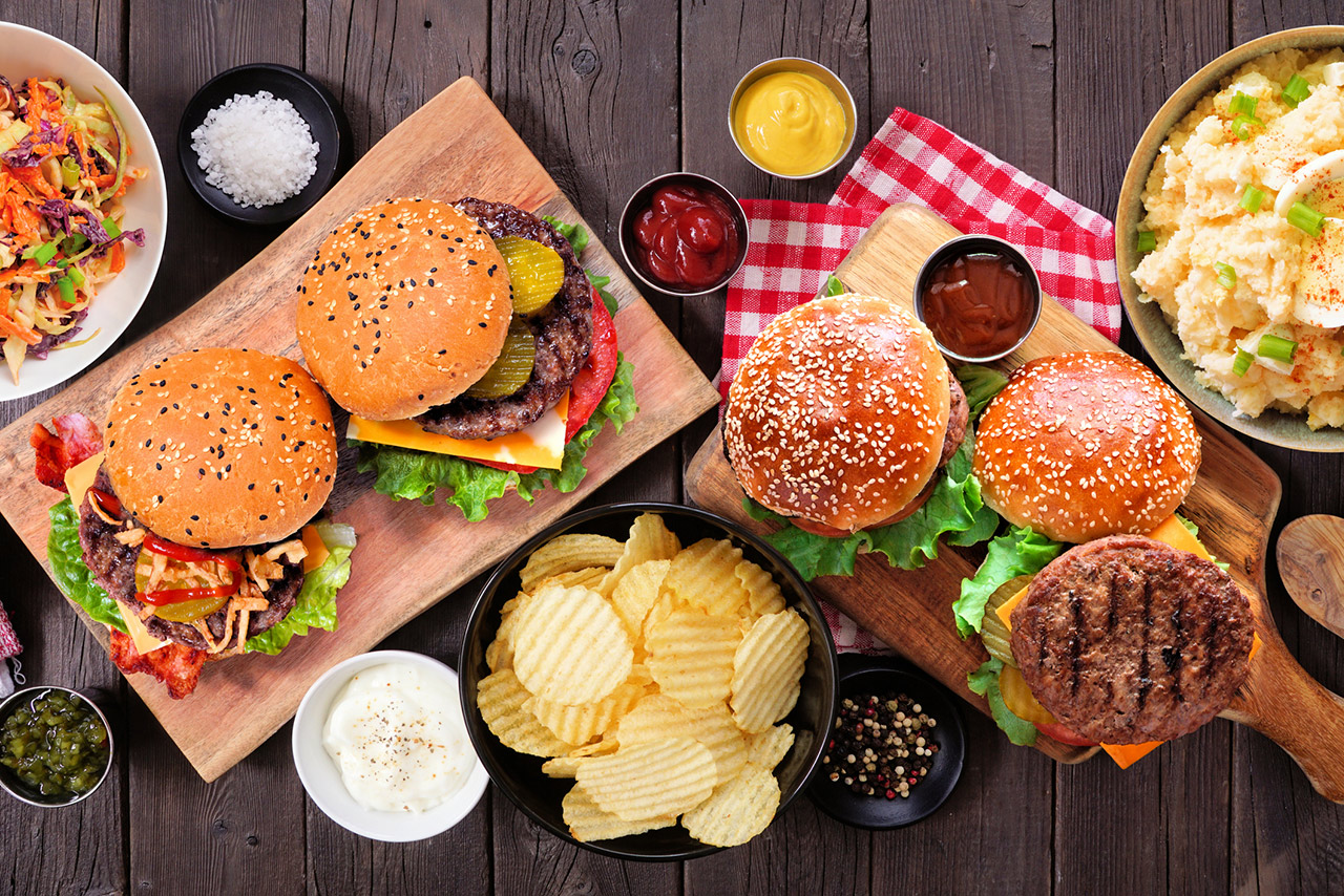 BBQ table scene with hamburgers, classic salads and snacks over dark wood stock photo
